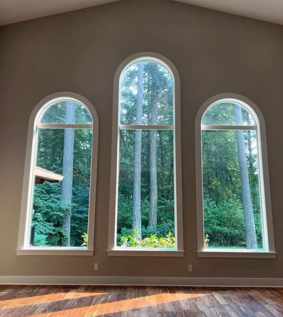 Three arched windows of graduated height looking into fir woods, with painted stools and aprons