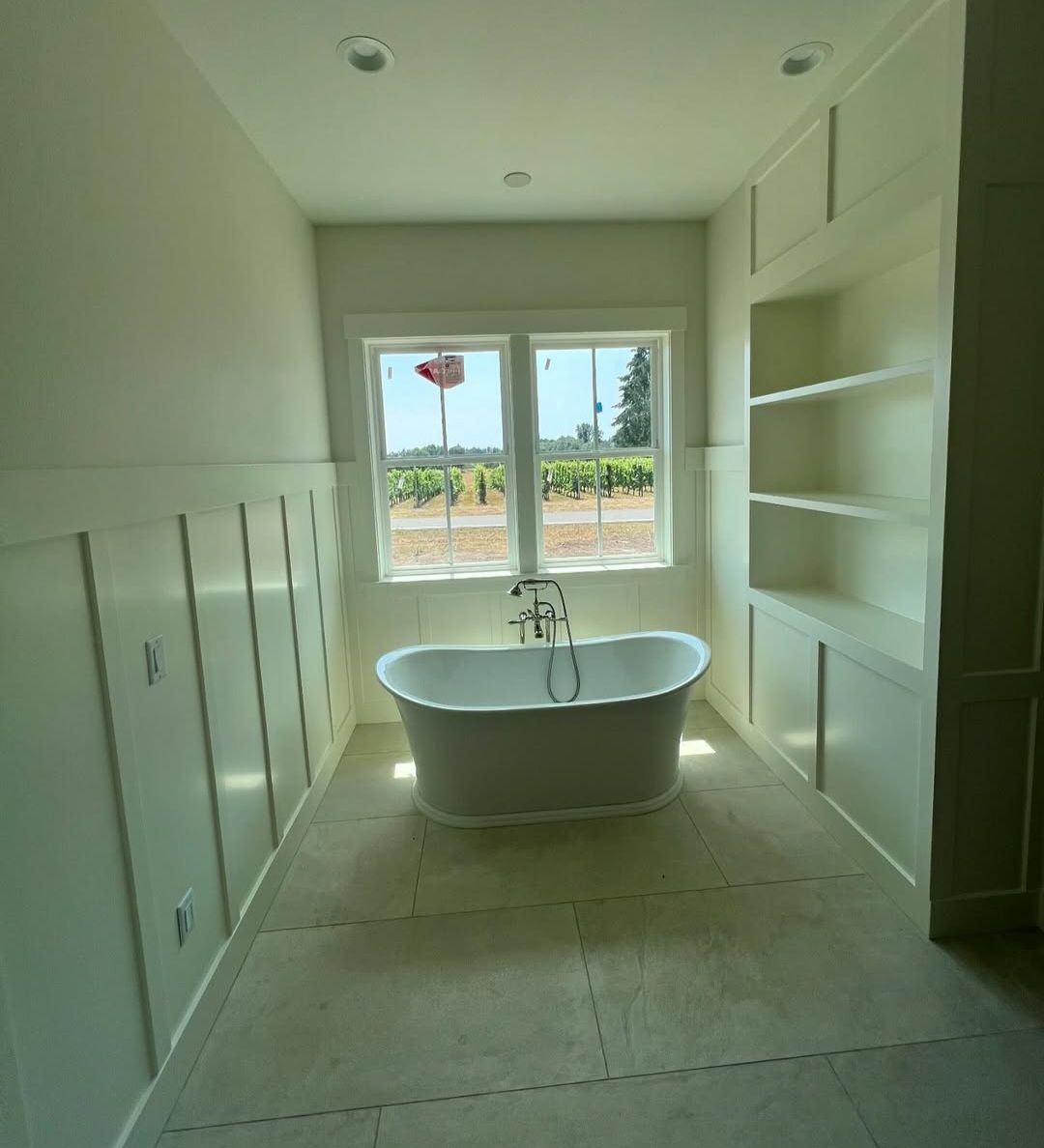 Master bath in board-and-batten with built-in shelving and a freestanding tub set under the window