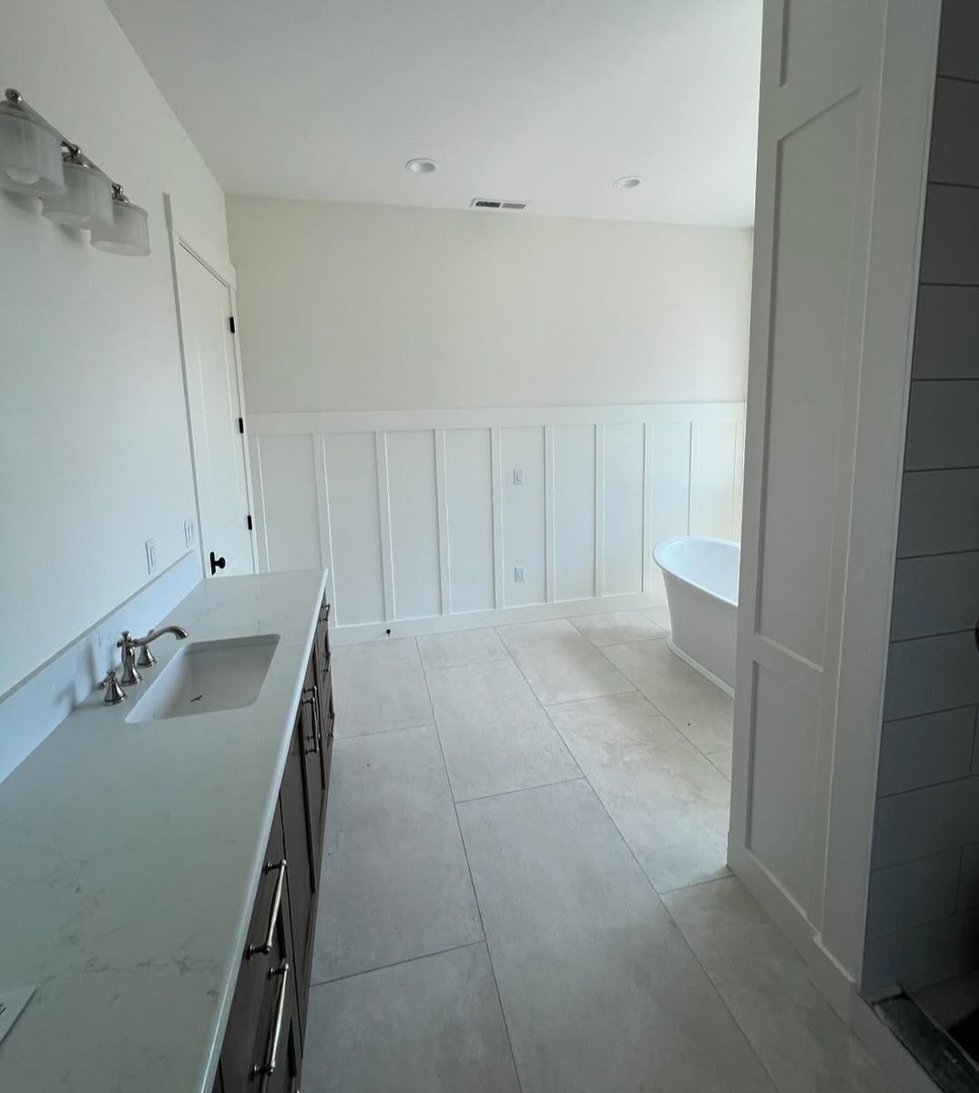 Master bath vanity run in quartz with a board-and-batten wall and freestanding tub beyond