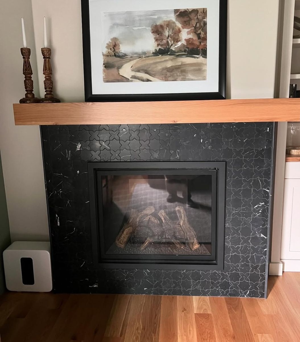 Fireplace faced in black star-and-cross tile with a solid cedar mantel and framed watercolour above