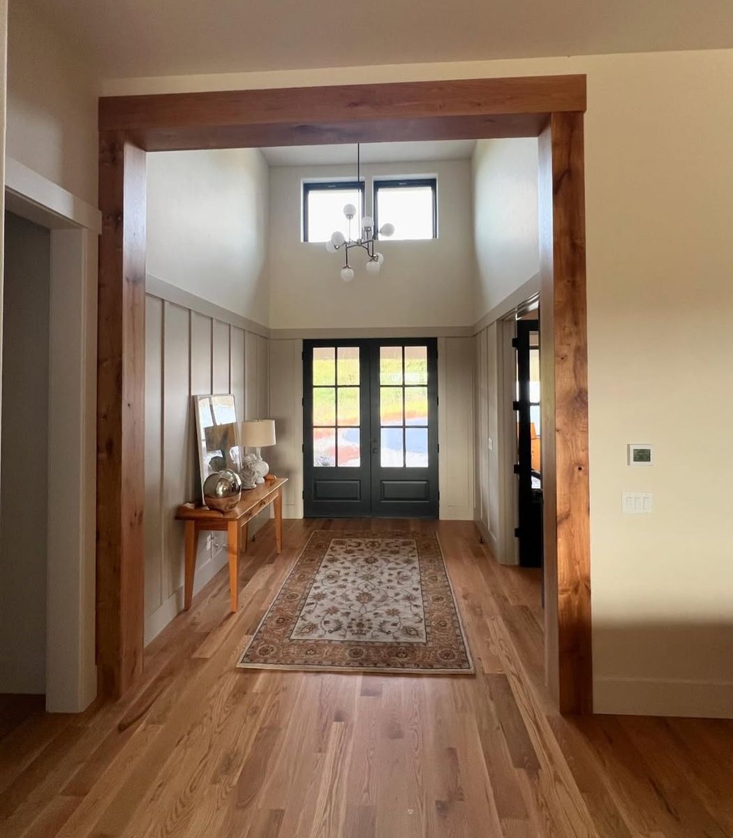 Entry hall framed by a rough-sawn timber opening, board-and-batten wainscot and black double doors with divided lights