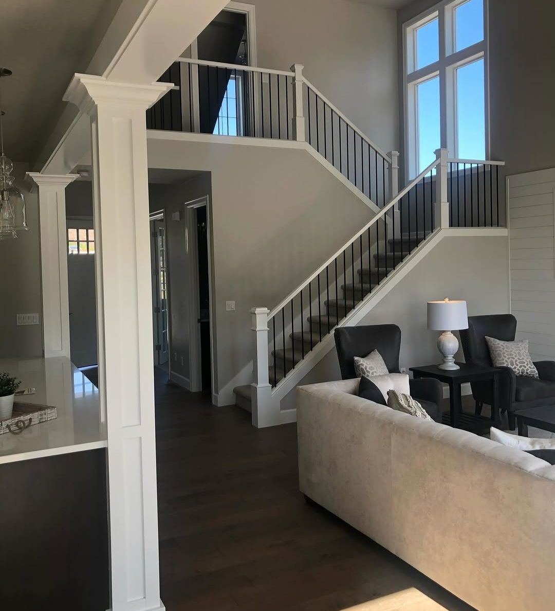Two-storey great room with a white craftsman staircase, square newel posts and black iron balusters, seen past a boxed column