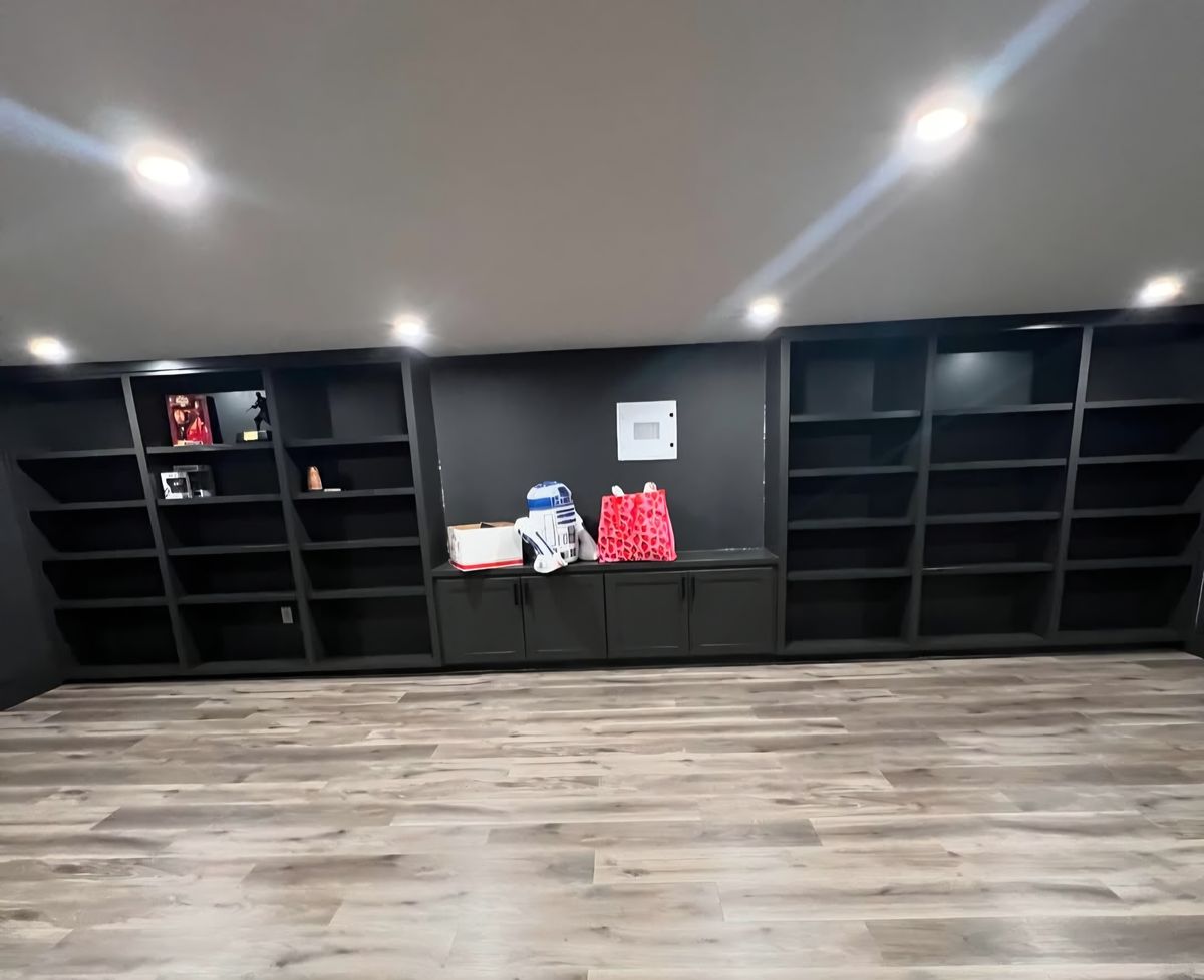 Full wall of black built-in shelving with a run of base cabinets and integrated lighting
