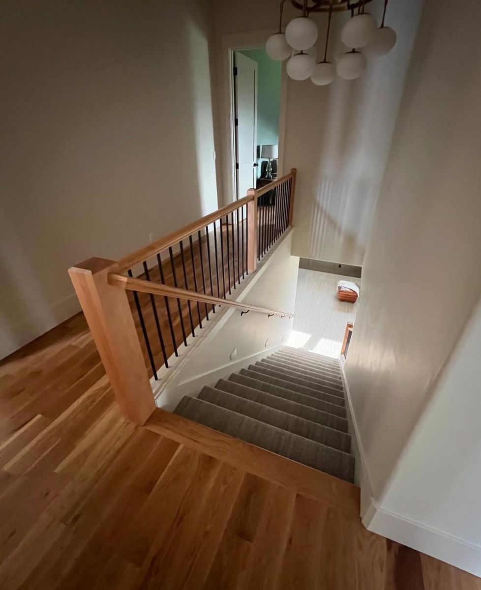 Looking down a stair run from the landing — hickory rail and newels with black iron balusters over oak floor