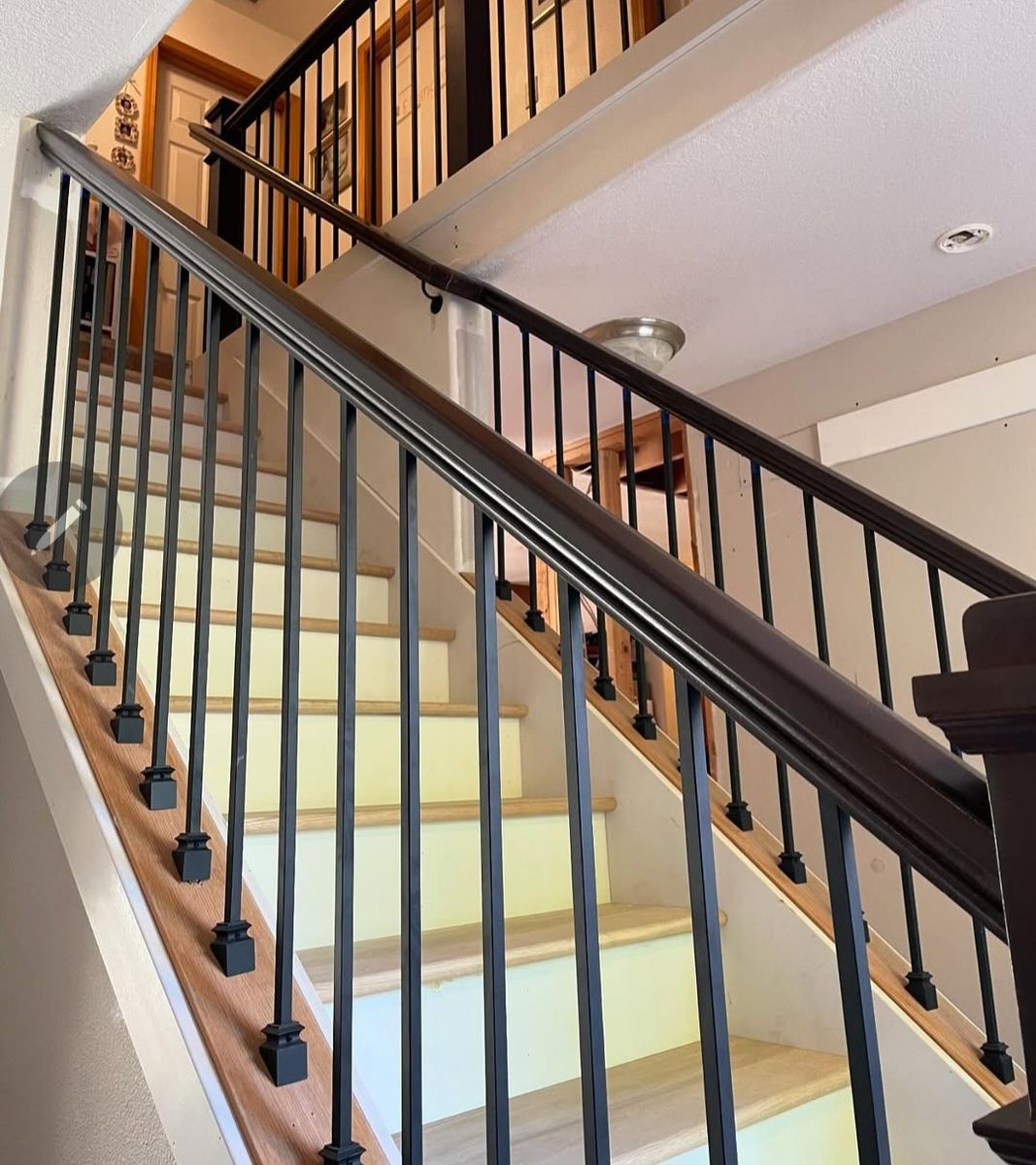 Close view along a stained rail and black iron balusters, with treads sanded ready for finish