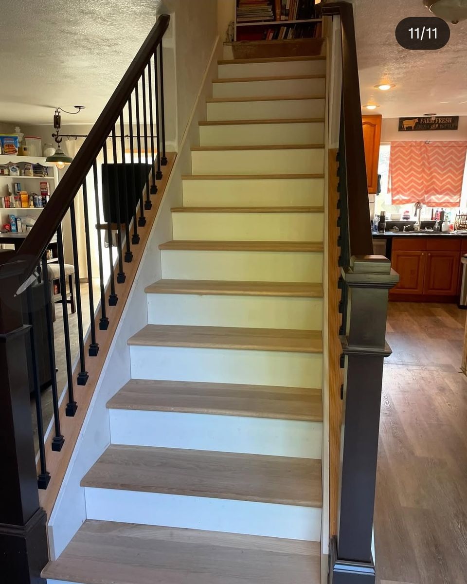 Stair remodel with new oak treads and painted risers, dark rail and iron balusters, opening onto a kitchen