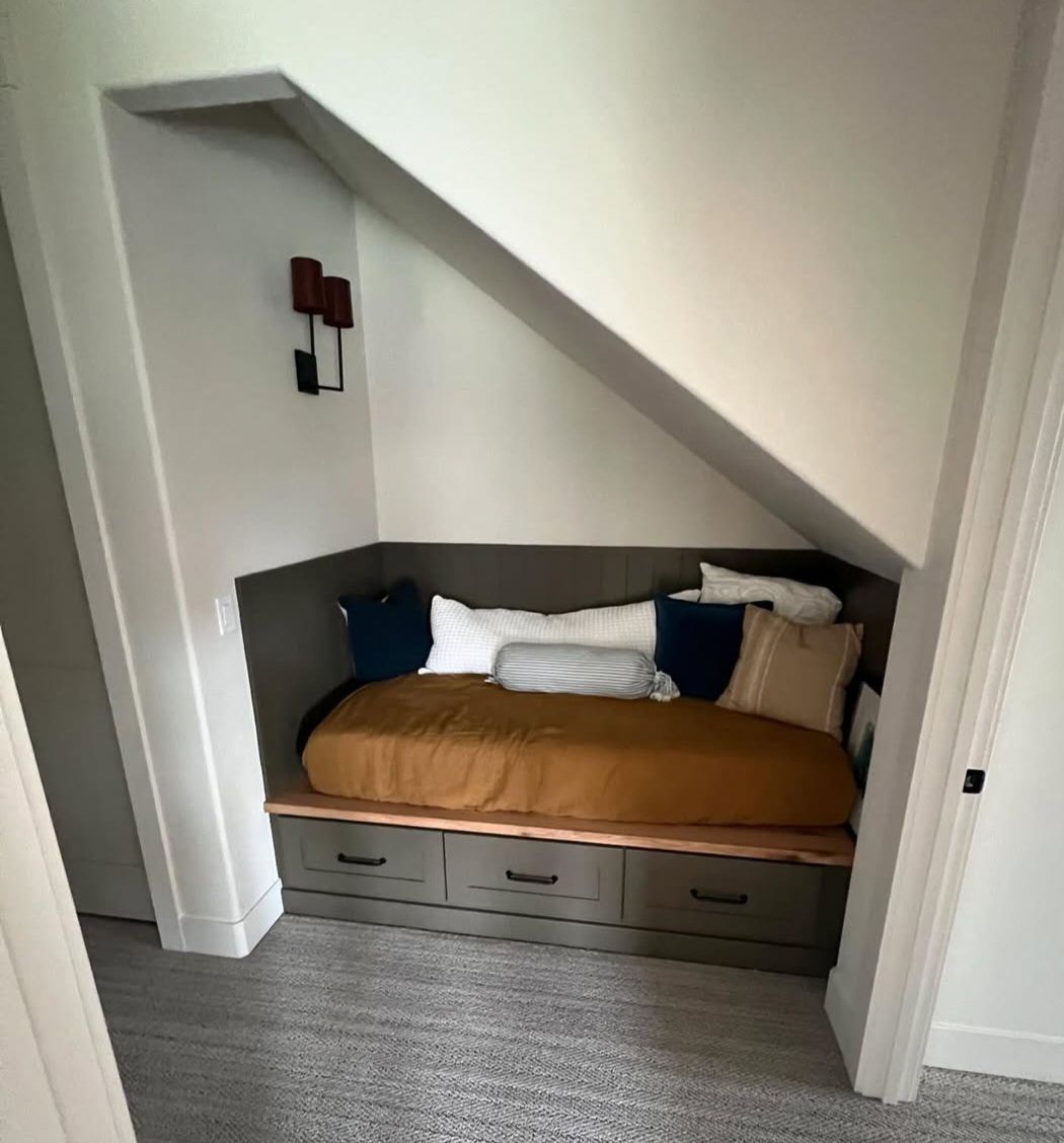 Built-in daybed tucked under a stair soffit, with shiplap back, live-edge ledge and three drawers below
