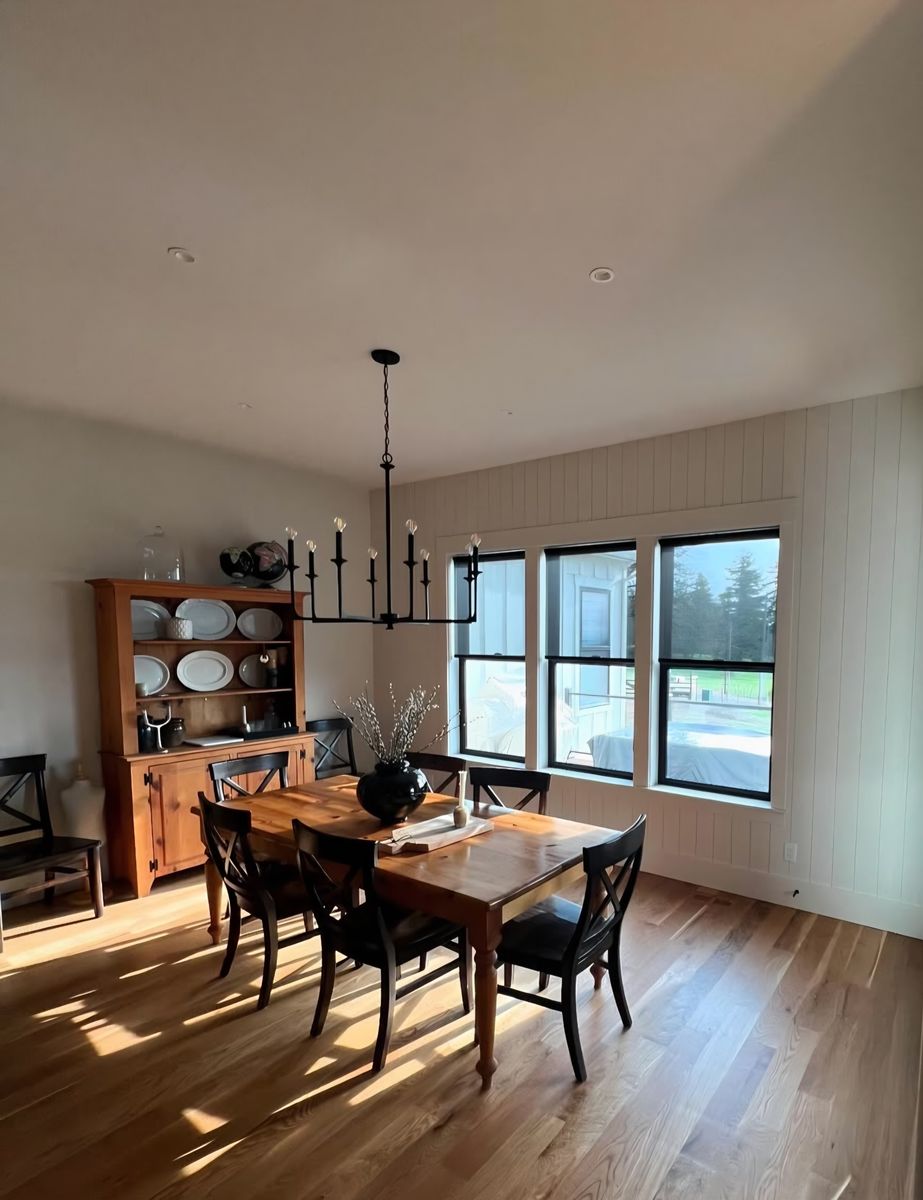 Dining room with vertical shiplap wainscot, black-framed windows and wide-plank oak floor in low sun